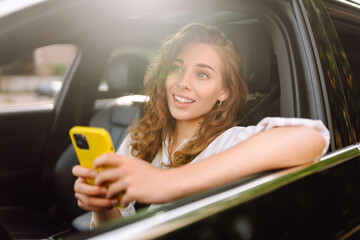 Young woman sitting in a car in the driver's seat looking into a smartphone, paying for parking and...