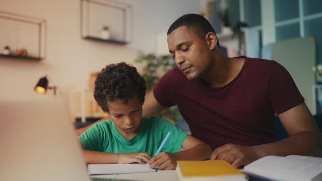 African American man aids son with homework, offering guidance in study