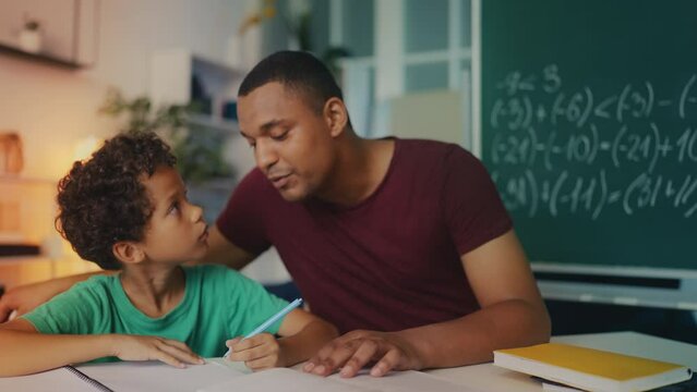 African American father helps son solve math equations, promoting homeschooling