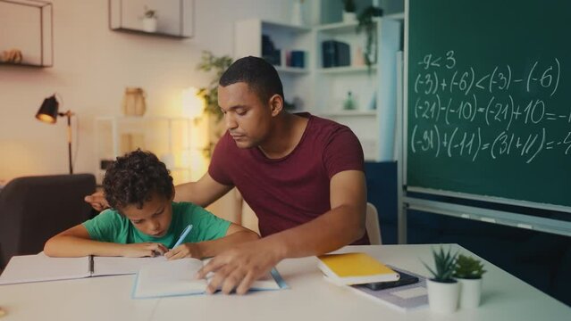 Father aids son with homework, boy writes math equations in his notebook