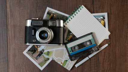 Old photo camera surrounded by photographs of women in different places, map, notebook and music cassette on a dark wooden table