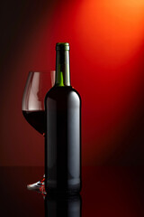 Glass and bottle of red wine on a red background.