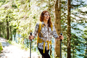 Young female traveler with hiking poles and a bright backpack. Healthy lifestyle eco tourism.