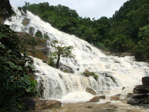 A majestic waterfall cascading down a lush green mountainside, surrounded by vibrant vegetation. The water plunges into a crystal-clear pool at the base of the falls.