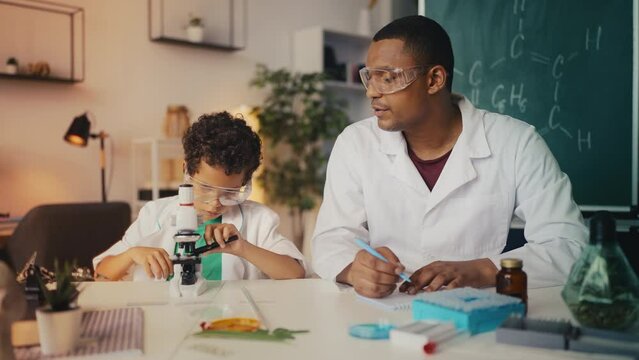 Boy in lab coat places sample under microscope, father documents test result