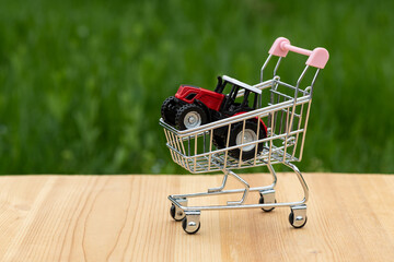 Miniature tractor in a shopping cart from a supermarket on a background of grass