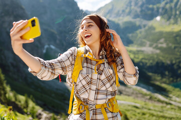 Tourist woman taking a selfie in nature on top of cliff with valley mountains view, sharing travel...
