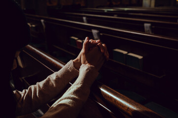 Close-up view of a woman's clasped hands as she prays in a church pew, emphasizing a personal and...