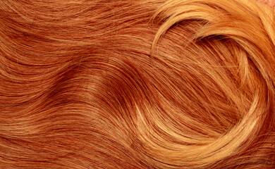Red hair close-up as a background. Women's long orange hair. Beautifully styled wavy shiny curls. Hair coloring bright shades. Hairdressing procedures, extension.