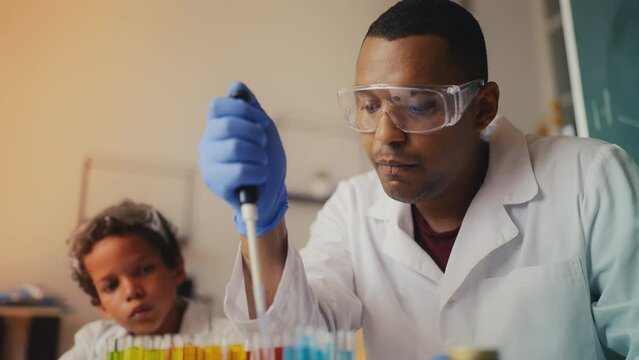 Father mixes test tube liquids with a lab pipette, teaching son chemistry