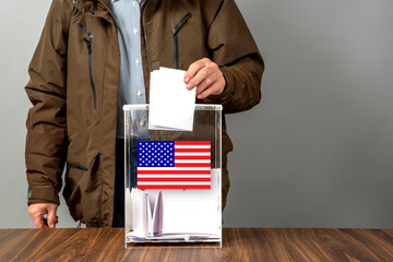 A voter casts a ballot into a ballot box on election day, USA flag