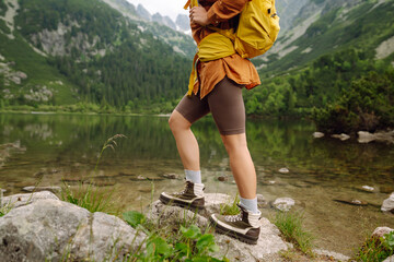 Woman traveler with yellow hiking backpack and hiking stiks enjoys the scenery. Active lifestyle. Wanderlust.