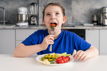 A little funny girl with a healthy breakfast puts tomato, spinach and cheese on a fork in her...