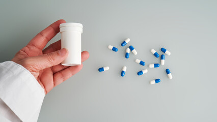 A hand holds a jar of white and blue pill on a blue background.