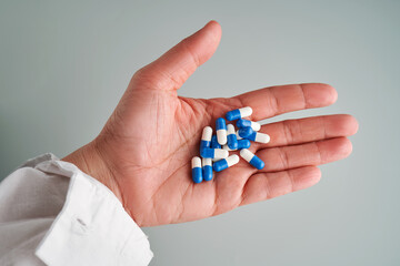 A hand holds a handful of white and blue pills on a blue background.