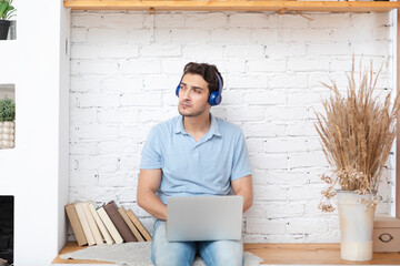 Young male student in headphones listening audiobook and reading in the same time. Online learning...
