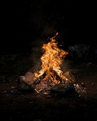 Naklejka premium A fire burning in the dark with rocks and a black background.