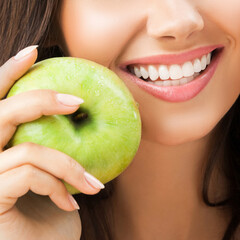 Close up image of toothy smiling happy woman with white teeth holding green apple. Brunette girl - optimistic, positive, dieting dental care, stomatology ad concept. Square composition.