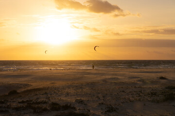 Windsurfers surfing in the Atlantic ocean next to Palomar beach in costa de la luz at sunset with bright sky and sand dunes