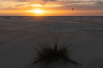 People surfing with kite at sunset on Palomar beach in Spain at sunset with sand dunes with vegetation on a sunset sky with bright colors