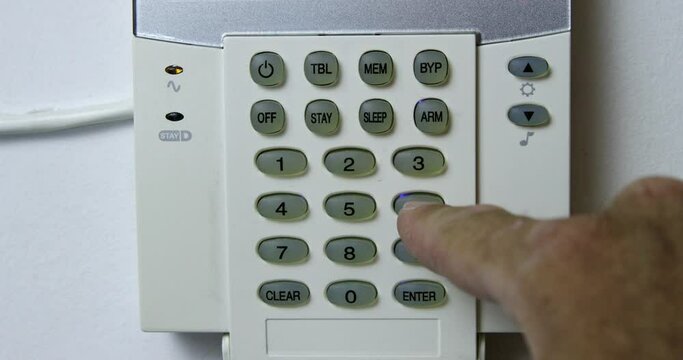 A mans hand is captured as he sets an alarm on a wall-mounted security keypad inside a house, ensuring safety and security.