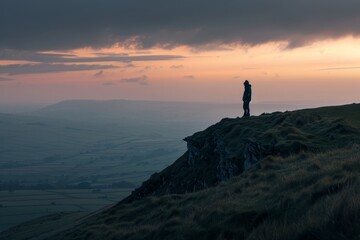 Fototapeta premium Individual standing on hill summit, gazing at setting suns glow, A lone figure standing on a hilltop, watching the evening descend with a sense of peace and contemplation
