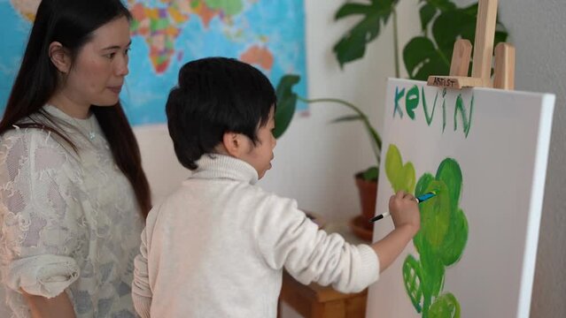 Asian teacher and little child painting on canva inside preschool class room- Mother and son doing art paint indoor - Creative activity and education concept 