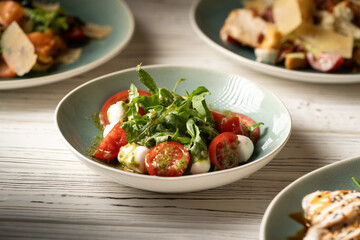 Italian caprese salad with tomatoes, mozzarella cheese, basil and olive oil serving on plate on...