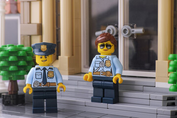 Naklejka premium Tambov, Russian Federation - May 10, 2024 A Lego policeman and a Lego policewoman minifigures standing in front of their police station.