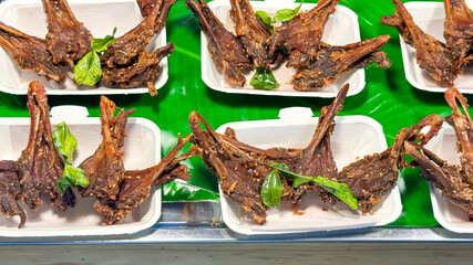 Crispy fried bats, garnished with basil leaves and arranged on foam trays over banana leaves....