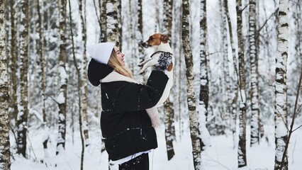A girl tosses up her Jack Russell Terrier dog in the woods in winter.