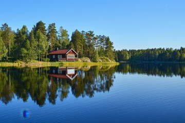 A house perched on the shore of a calm lake under a clear blue sky, A peaceful lakeside retreat, with a clear blue sky reflected in the water