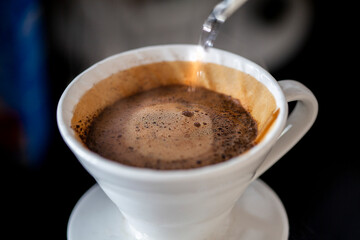 The moment hot water is being poured over coffee grounds in a white ceramic pour-over coffee maker