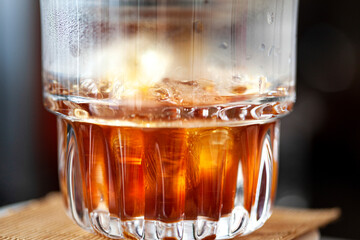 A close-up of a glass of iced tea, highlighting the rich amber color of the tea and the light refracting through the liquid and ice cubes