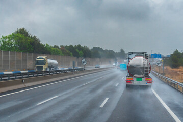 Trucks and other vehicles driving on a highway on a rainy day, reducing visibility due to the water...