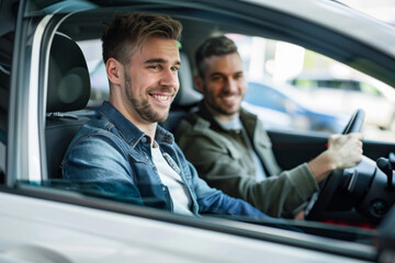 A young man is sitting in the car and smiling while his friend, who works at an auto dealership, shows him various details of a white modern family car
