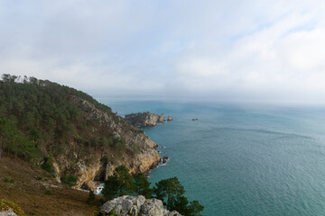 Sous un ciel couvert, la Pointe Saint-Hernot garde son charme sauvage. Les falaises se dressent, les eaux murmurent. Une beauté mystique persiste.