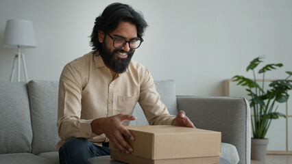 Happy male customer client consumer Arabian indian man guy in glasses open cardboard box at home...
