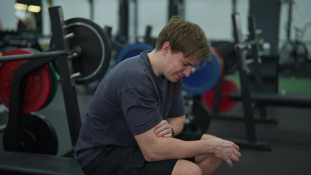Exhausted beginner sportsman having accident injury and hurt at arms while workout and weight training at gym. Athletic man suffering from muscle injury while exercising at sport club, slow motion.
