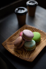 Multicolored macarons in a wooden plate and two cups with coffee in dark colors