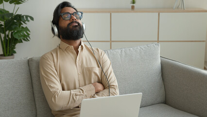 Arabian ethnic businessman working online with laptop tired stressed Indian exhausted business man listen chill music in headphones on mobile phone eyes closed stress free break relax in home office