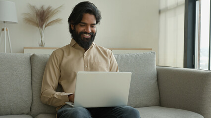 Arabian muslim man freelancer working from home focused millennial guy indian businessman typing on computer laptop surfing internet looking at screen sitting on couch distant remote job on quarantine