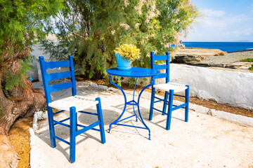 Two blue chairs and table in courtyard of Chrysopigi monastery with sea in background, Sifnos...