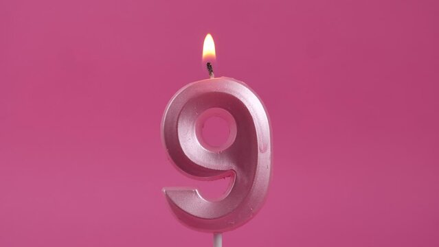 burning candle with number 9 on a pink background. birthday party
