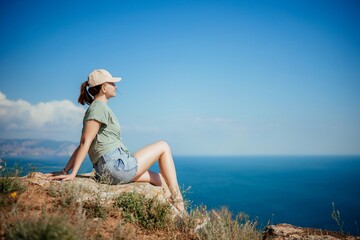 A woman is sitting on a rock overlooking the ocean