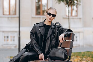 Stylish young woman with black sunglasses on her eyes, wearing a  t-shirt, a black leather jacket,...