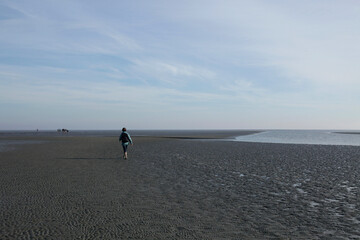 A woman walks across the mudflats of the Waddensea at low tide, Holland