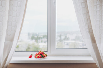 Fresh red strawberries on a plate on a white window with natural light. 