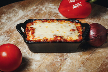 Baked Lasagna in a Black Ceramic Dish Surrounded by Fresh Vegetables