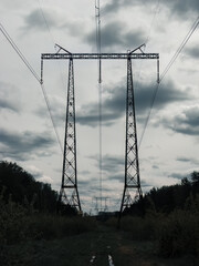 silhouette of high voltage power lines against cloudy sky.